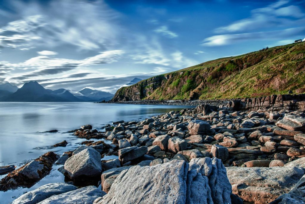 Serene coastal view with rocky shoreline and distant mountains under a vivid blue sky.
