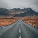 A scenic empty road stretches into snow-capped mountains under cloudy skies, offering a sense of adventure and tranquility.